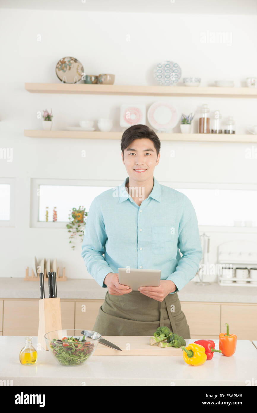 Sorridente giovane uomo in grembiule azienda tablet fissando davanti in cucina Foto Stock