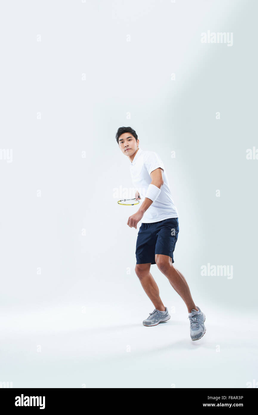 Uomo in abbigliamento sportivo e permanente di oscillazione di una racchetta da tennis con una mano fissando sulla parte anteriore Foto Stock