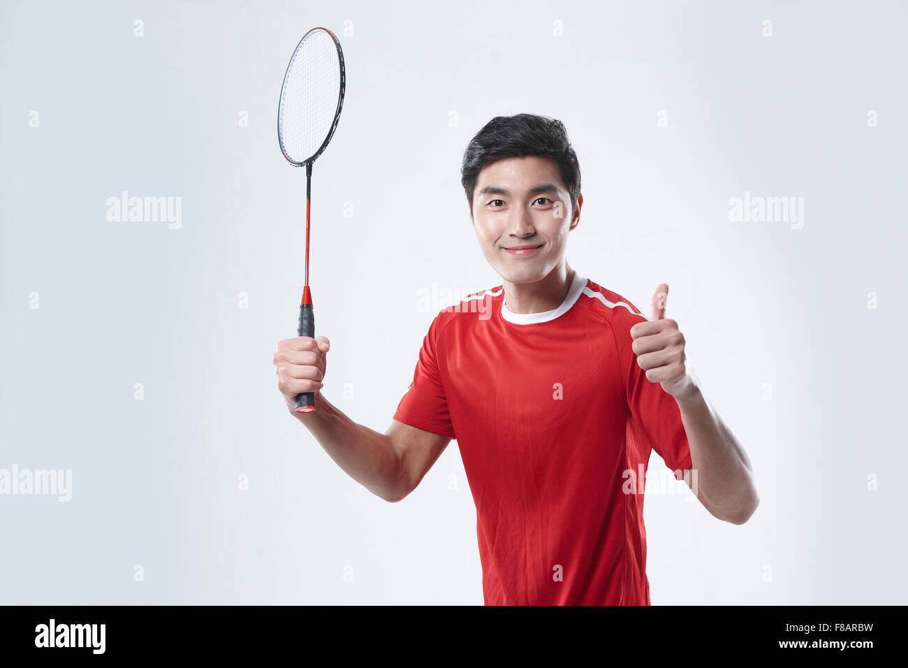 Ritratto di uomo con un campo di badminton racchetta e mostrando il pollice fino a firmare lo sguardo sul lato anteriore Foto Stock