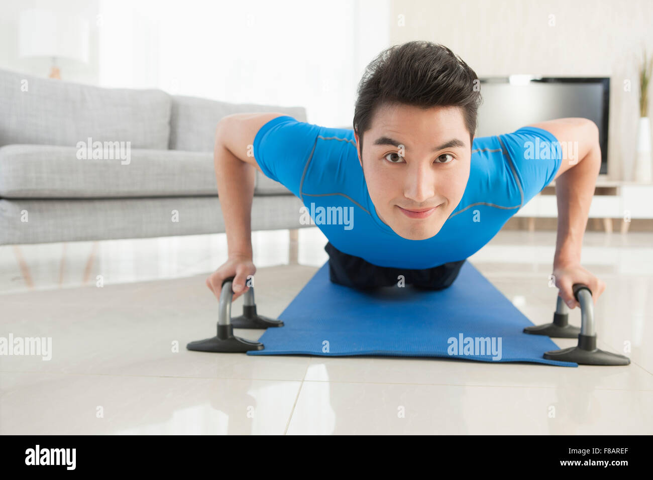Uomo disteso a faccia in giù e facendo push-up staring anteriore nel soggiorno Foto Stock