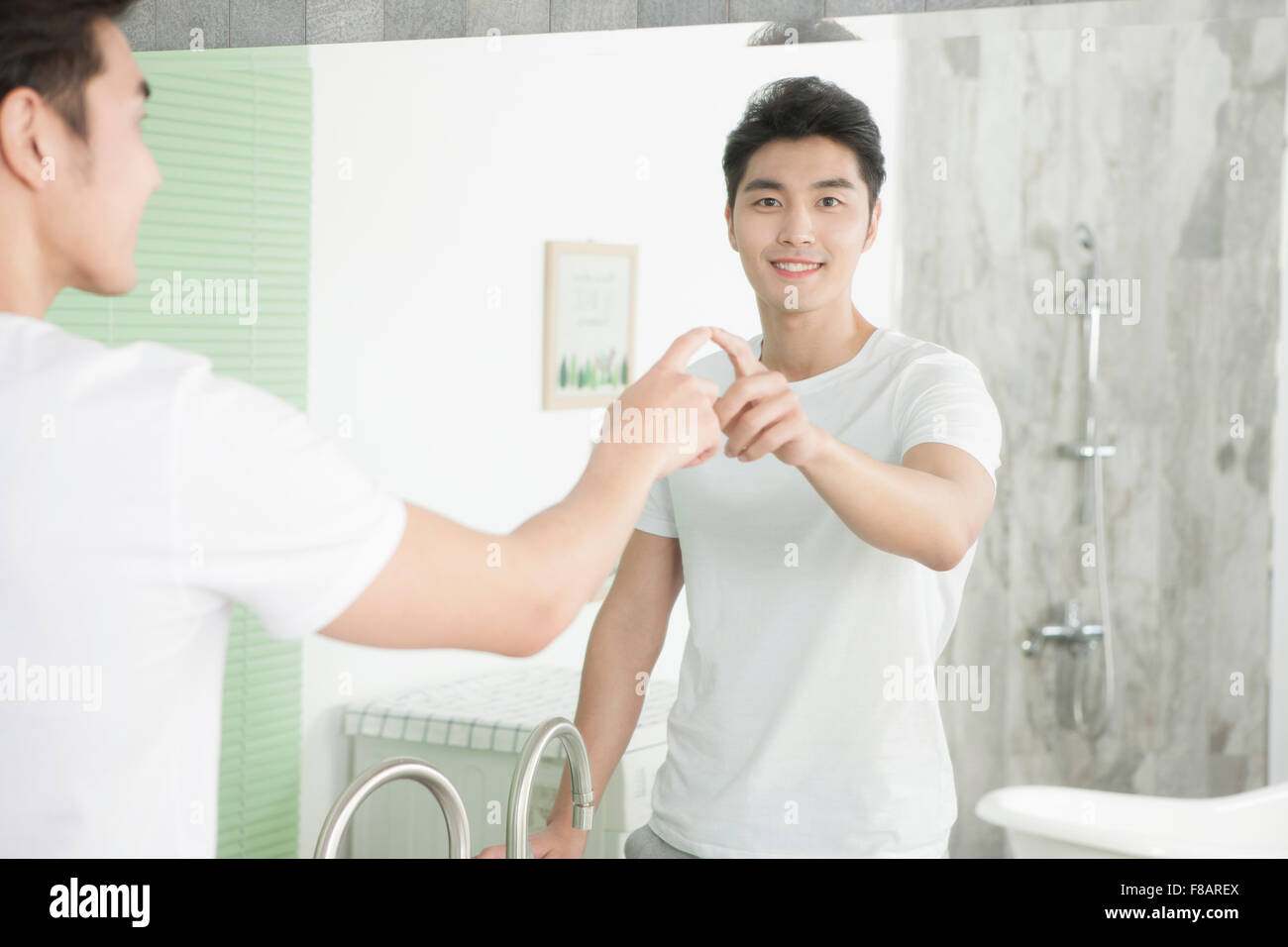Ritratto di giovane uomo di toccare se stesso fissando davanti con un sorriso a specchio nella sala da bagno Foto Stock
