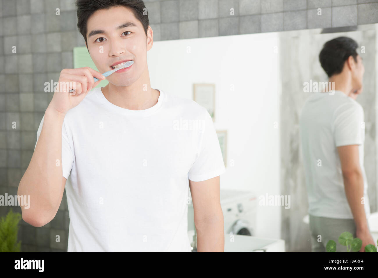Ritratto di giovane di spazzolare i denti in bagno lo sguardo sul lato anteriore Foto Stock