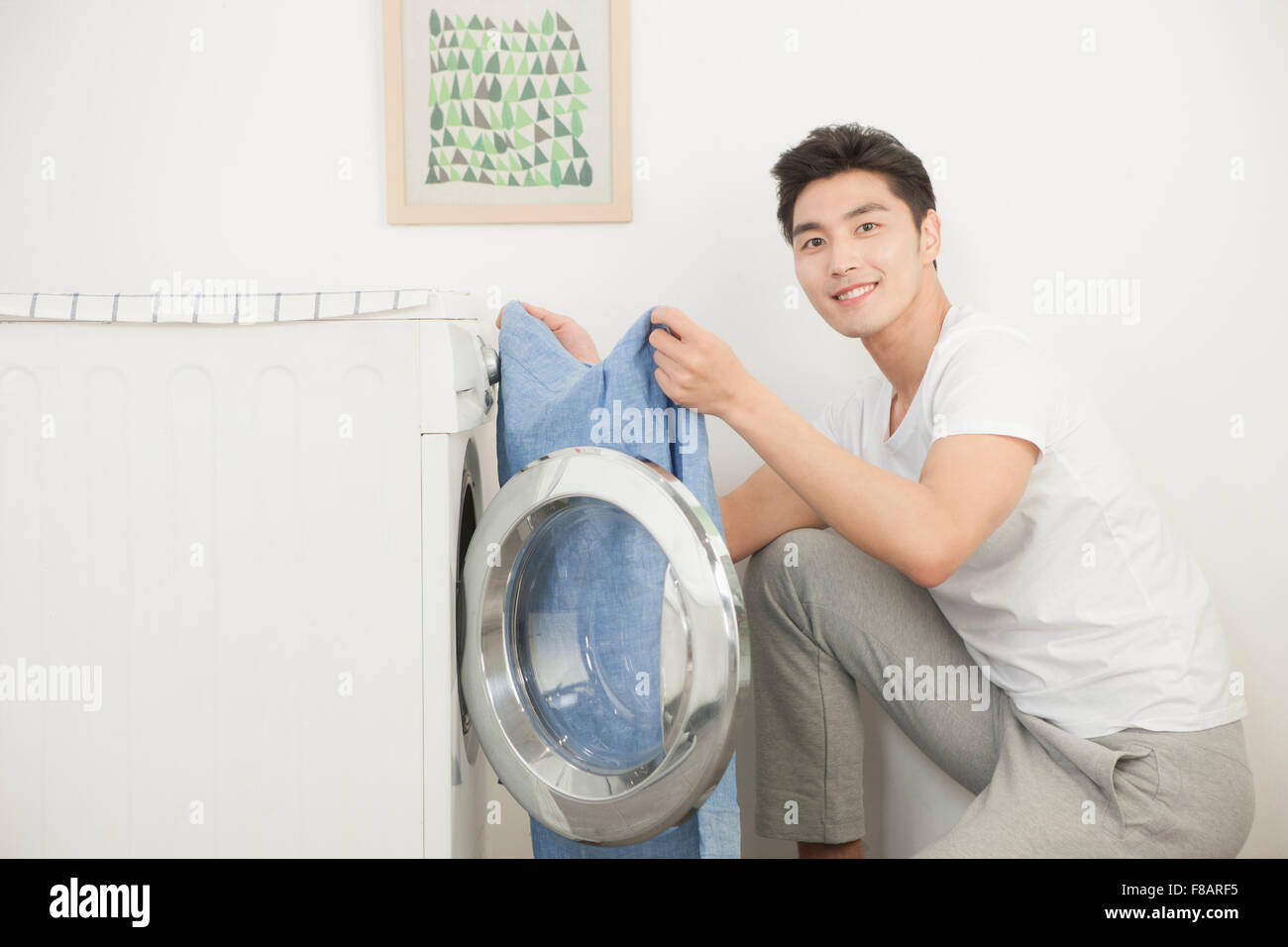 Giovane uomo prendendo la biancheria dalla macchina di lavaggio fissando davanti con un sorriso Foto Stock