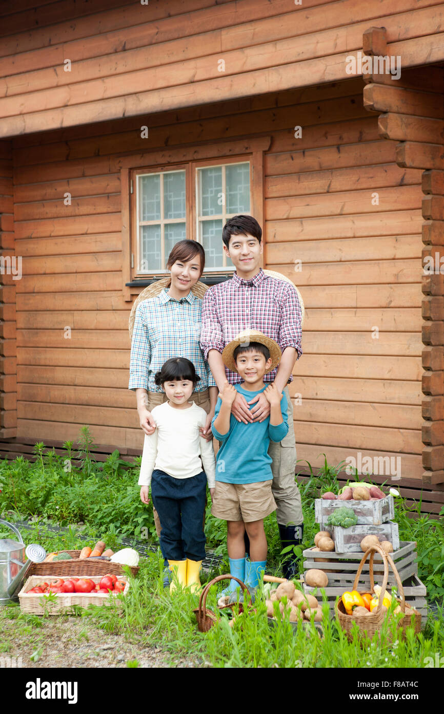 La famiglia felice in piedi con verdure fresche nella parte anteriore della casa di campagna con lo sguardo sul lato anteriore Foto Stock