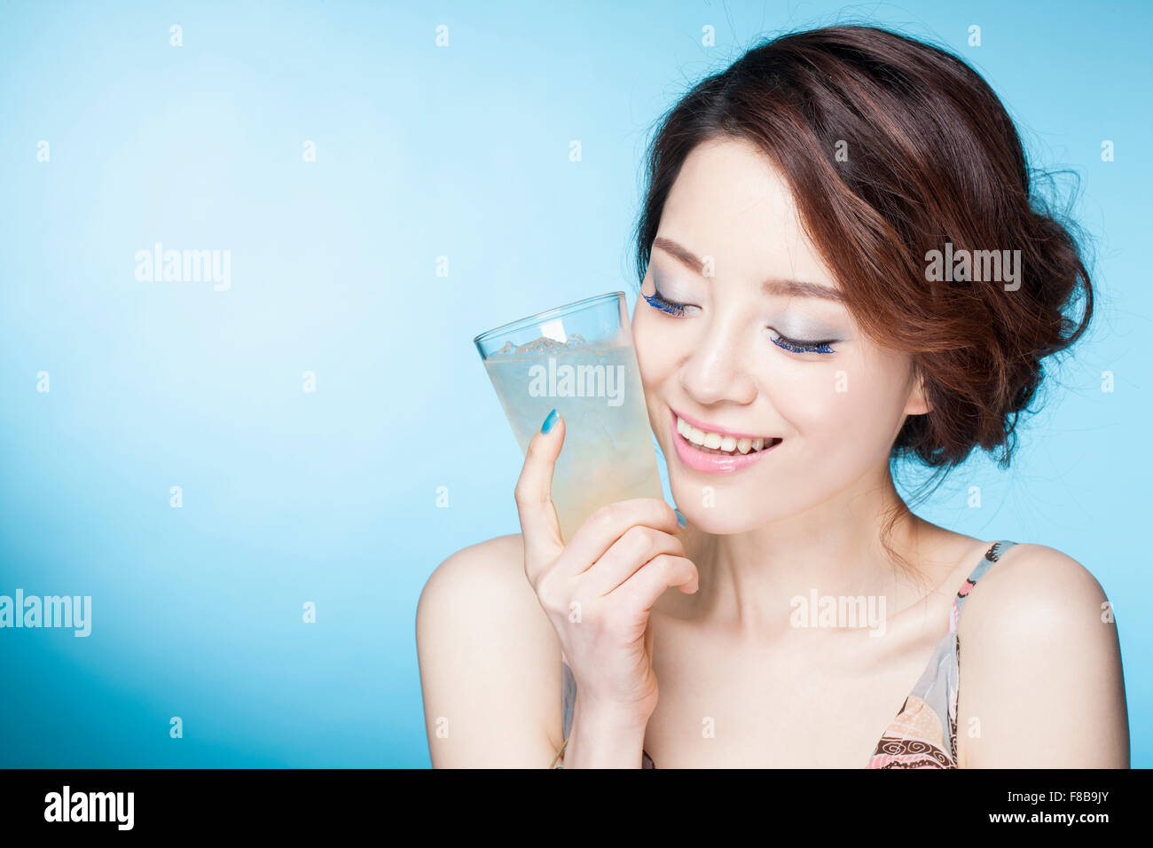 Donna in abiti estivi tenendo un bicchiere di bibita vicino al suo volto sorridente e con gli occhi chiusi Foto Stock