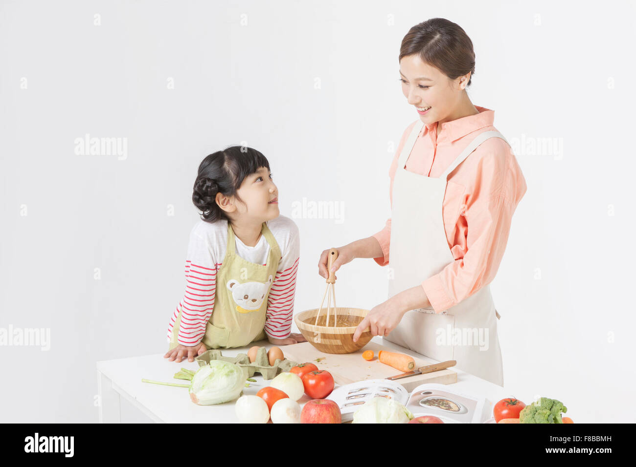 Madre e figlia in grembiuli cucina insieme al tavolo e guardando a vicenda con un sorriso Foto Stock