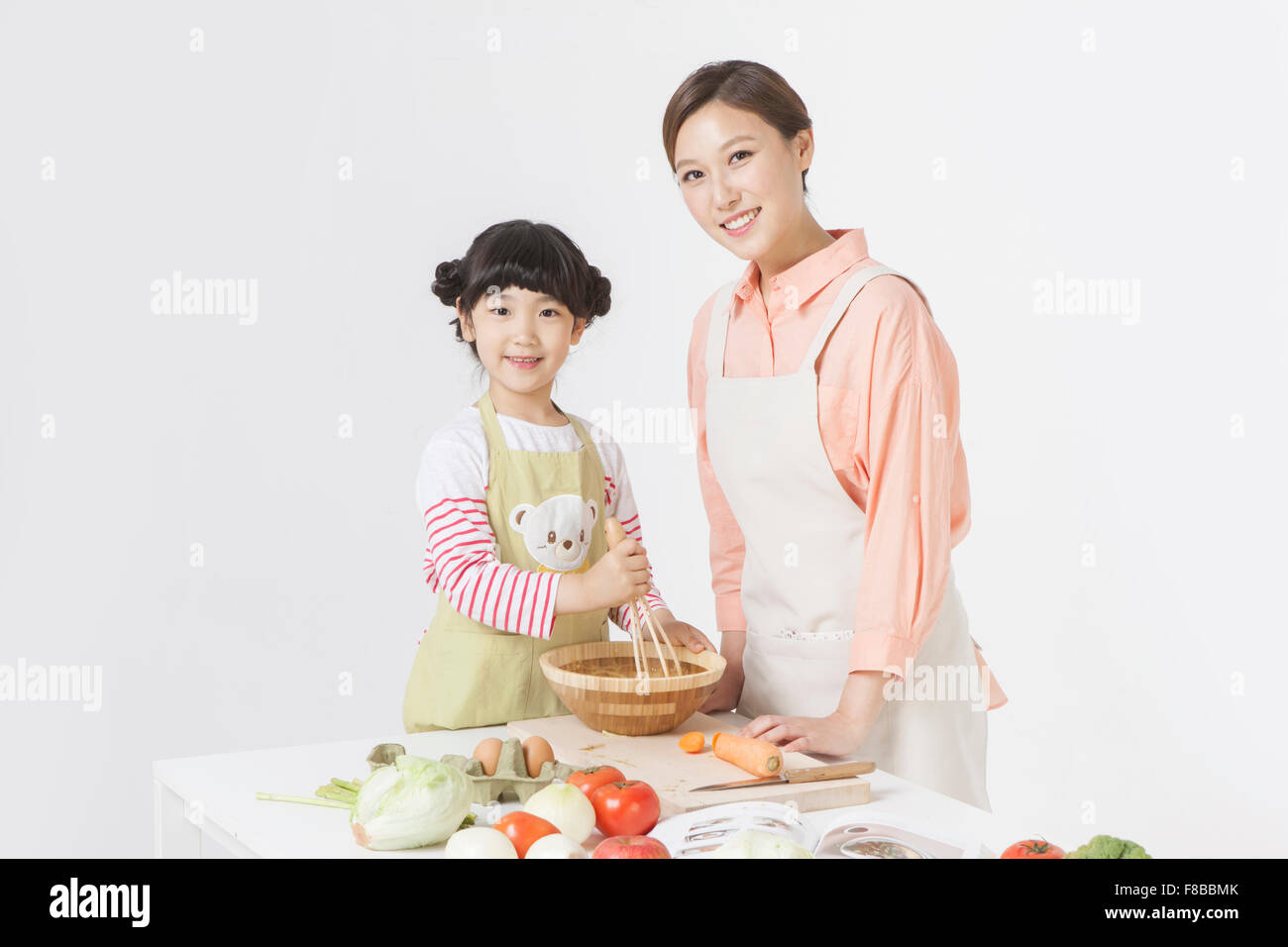 Madre e figlia in grembiuli cucina insieme a tavola e con lo sguardo in avanti con un sorriso Foto Stock