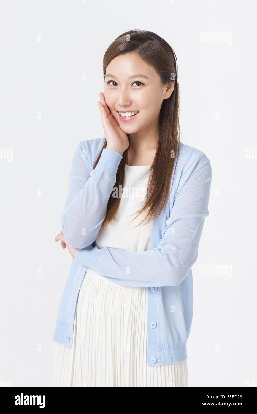 Donna in abito bianco e blu cardigan mettendo la sua mano sul suo viso e sorridente Foto Stock