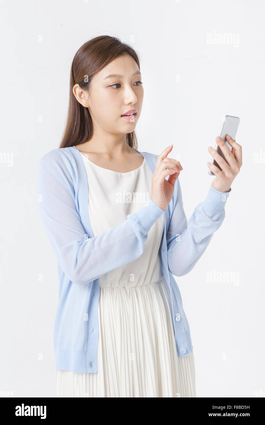 Donna in abito bianco e blu cardigan tenendo un smartphone e lo sta guardando Foto Stock
