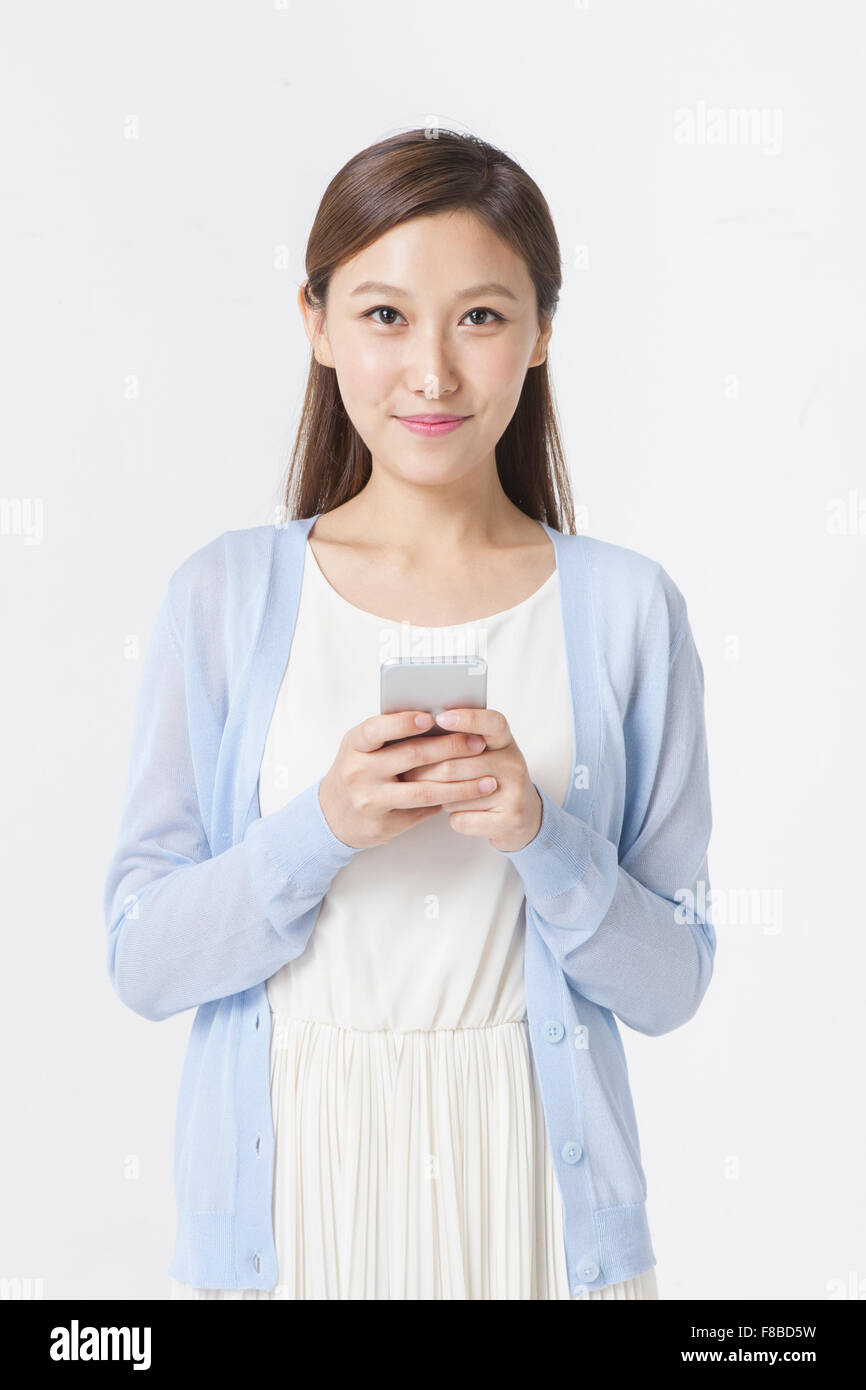 Donna in abito bianco e blu cardigan con lo sguardo in avanti con uno smartphone e sorridente Foto Stock