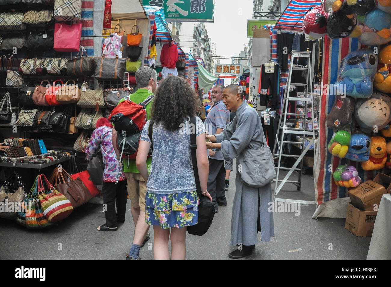 'Monk' accattonaggio da turisti caucasica nel mercato di Hong Kong come tour guida spiega circa 'falso' accattonaggio monaci Foto Stock