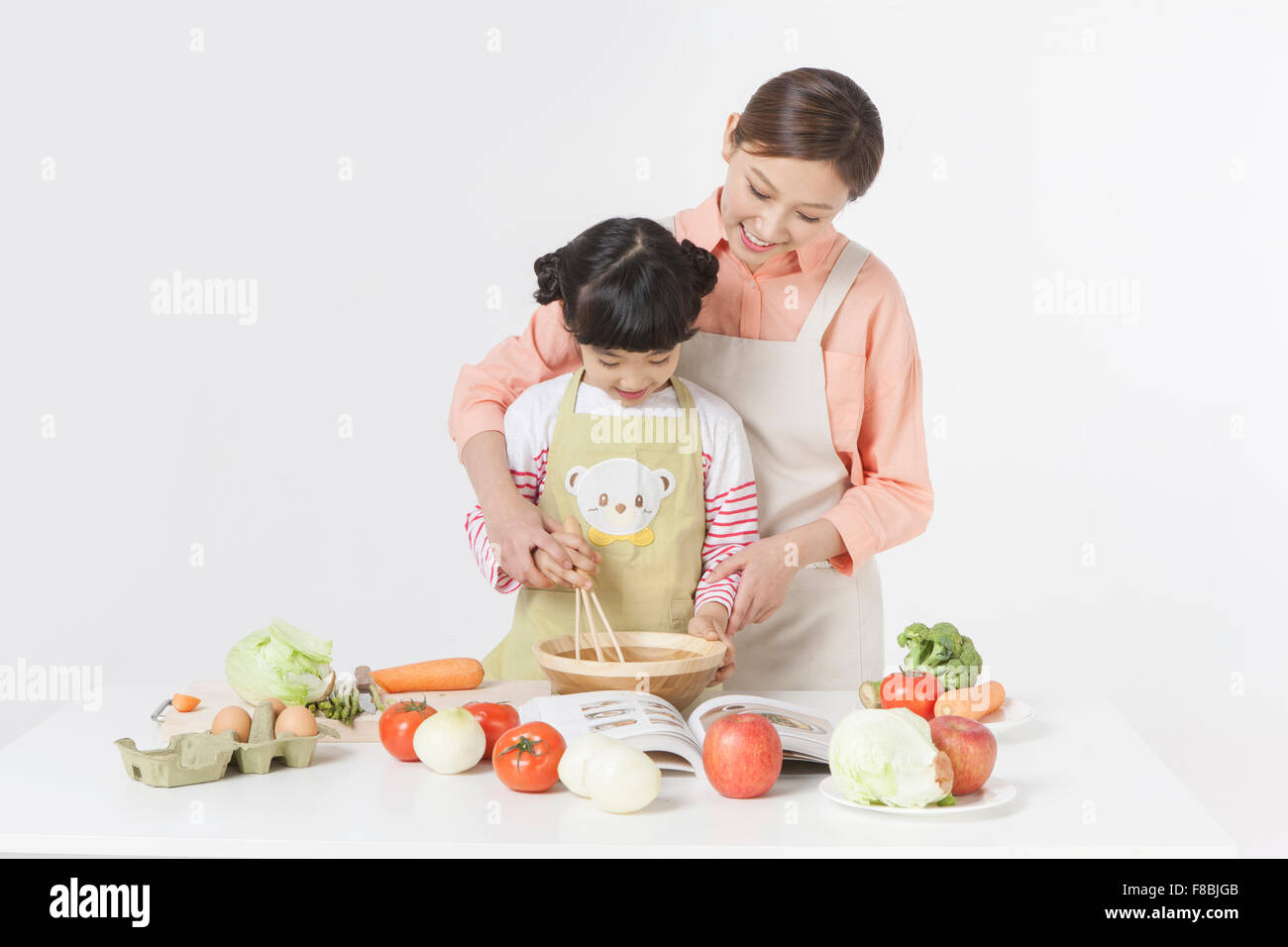 Madre e figlia cucina insieme con una varietà di verdure e altri ingredienti alimentari messi sul tavolo Foto Stock