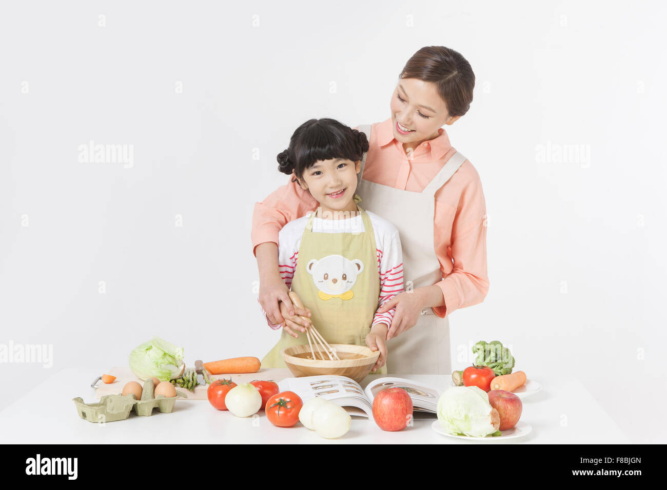 Madre e figlia cucina insieme con una varietà di verdure e altri ingredienti alimentari messi sul tavolo Foto Stock