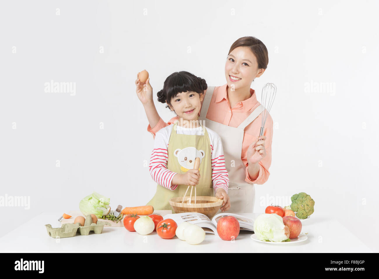 Madre e figlia cucina insieme con una varietà di verdure e altri ingredienti alimentari messi sul tavolo Foto Stock