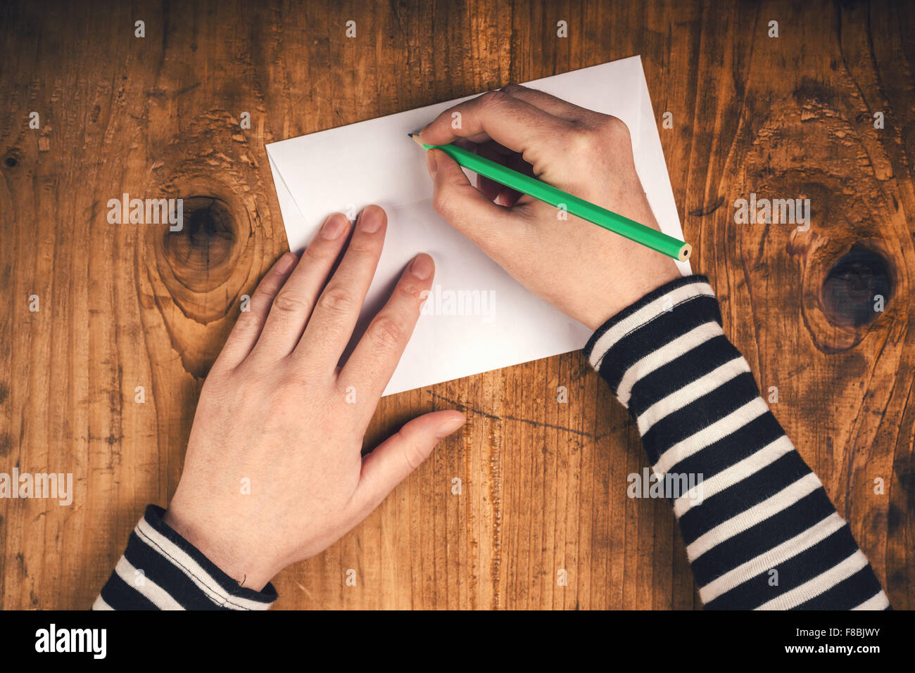 Donna scrivere l'indirizzo del mittente sulla busta postale, mani femminili dal di sopra sulla scrivania in ufficio invio di lettera, vista dall'alto, dai toni rétro. Foto Stock