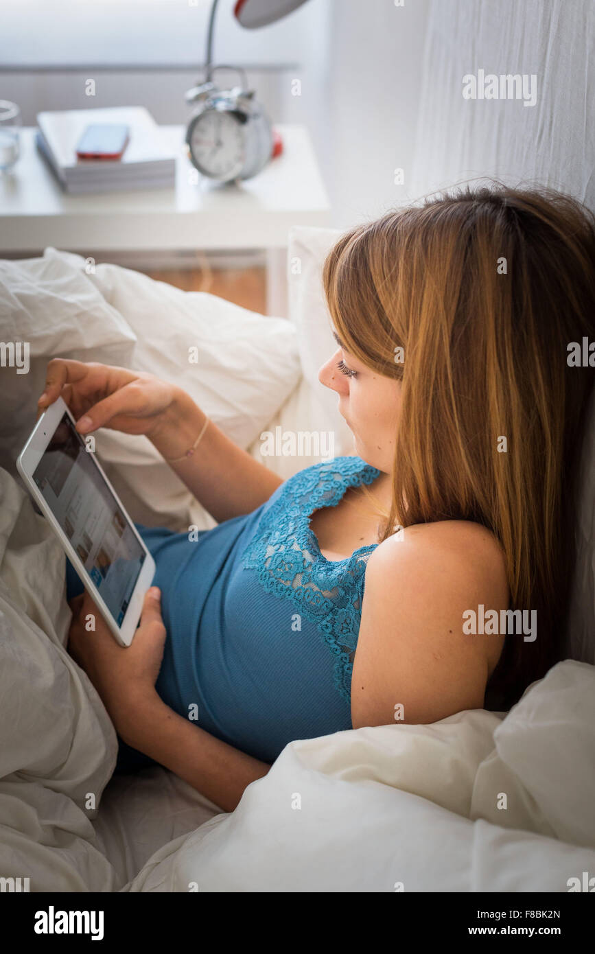Donna che utilizza una tavoletta digitale giacente in letto. Foto Stock