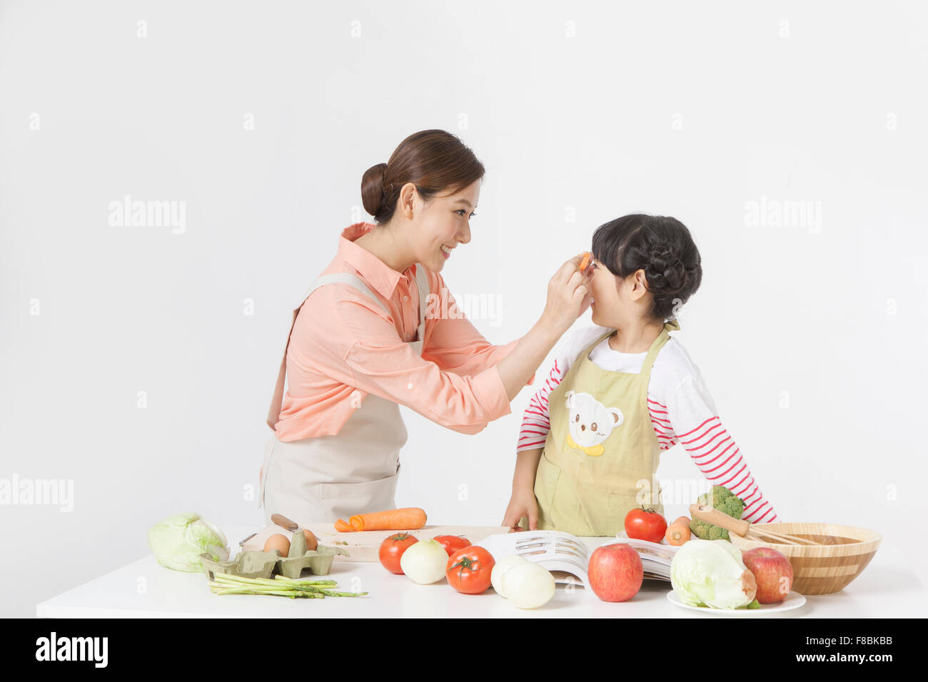 Azienda madre fette di carota e metterli vicino a sua figlia del volto sia in grembiule e gustando la cucina insieme Foto Stock