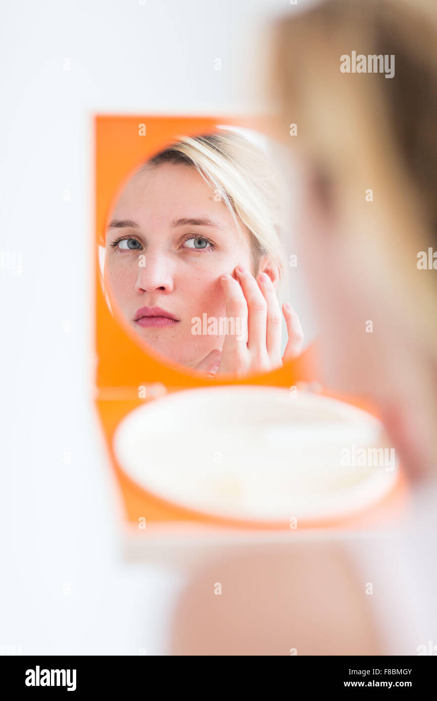 Donna controllando la sua faccia nello specchio. Foto Stock