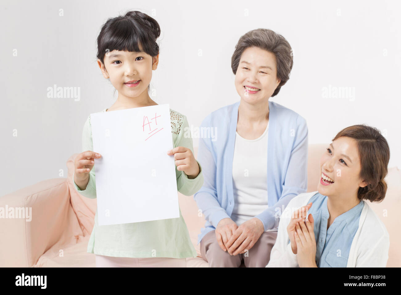 Giovane ragazza tenendo un plus di prova di grado di risultato e di sua madre e nonna di essere felice, guardando il suo Foto Stock