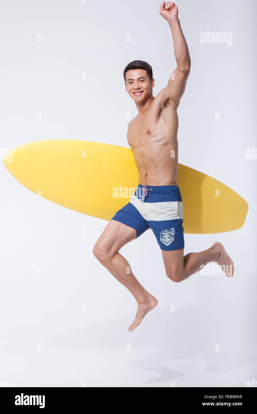 Uomo muscolare tenendo un surf board sotto il suo braccio e salto con la sua mano alta Foto Stock