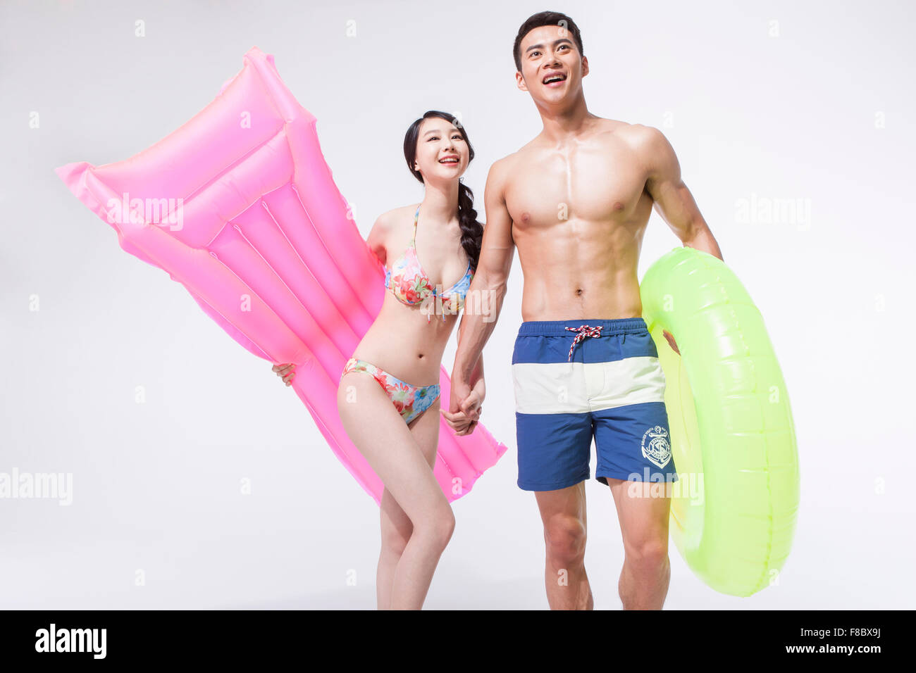 Donna in bikini tenendo un galleggiante rosa sotto il suo braccio e un uomo in pantaloni di nuoto tenendo un tubo ad anello sia con lo sguardo verso l'alto Foto Stock