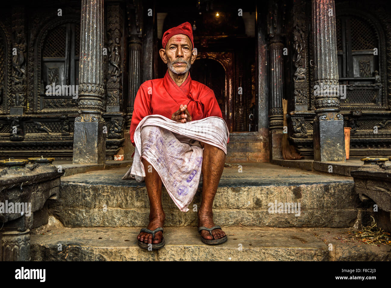 Il vecchio monaco buddista seduto di fronte al suo tempio di Kathmandu Foto Stock