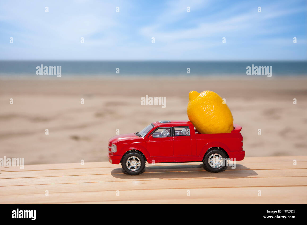 Auto in miniatura che trasportano un limone sul materiale di legno con lo sfondo della spiaggia Foto Stock