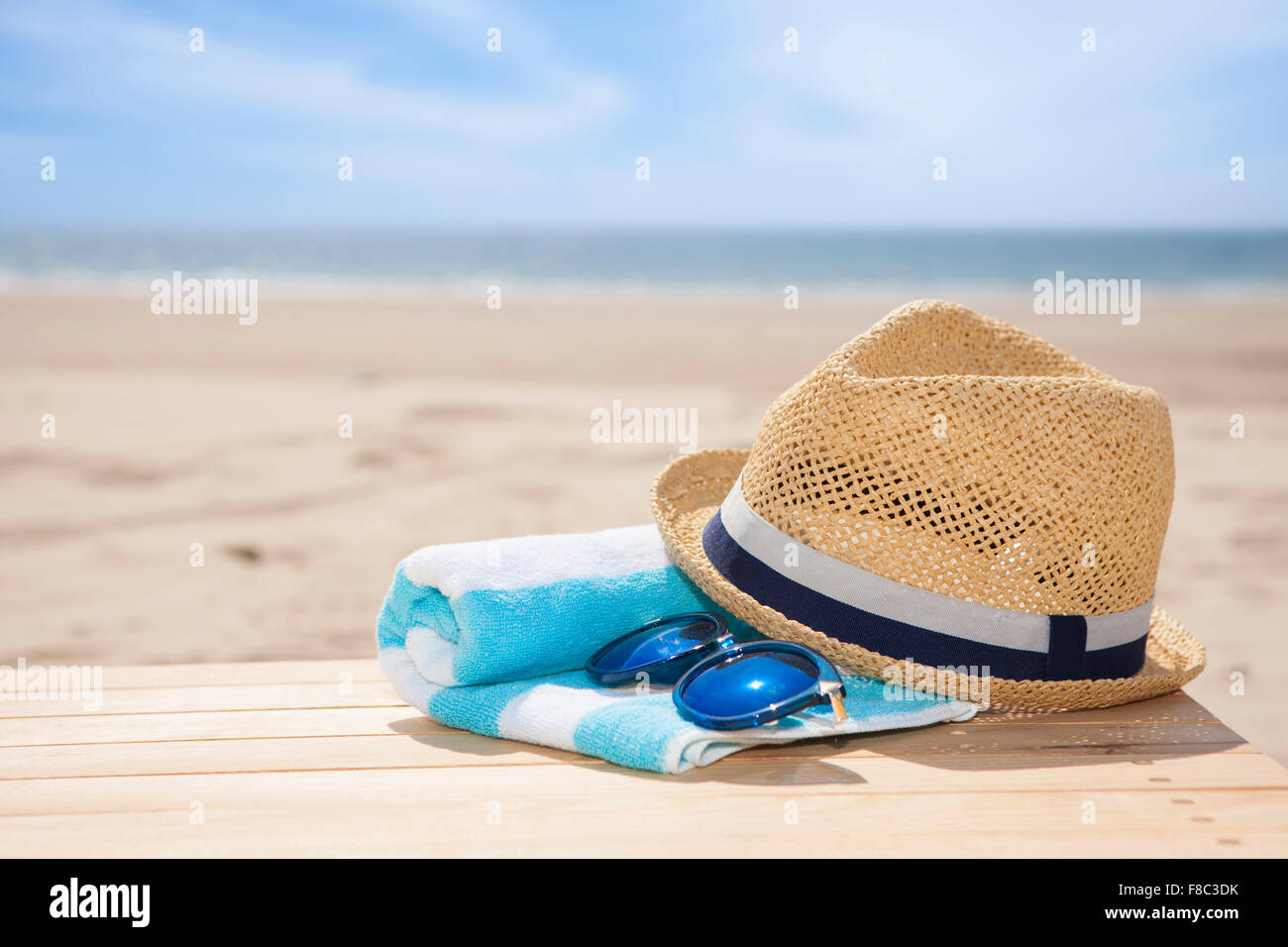 Cappello, occhiali da sole su asciugamani su materiale di legno al di fuori della messa a fuoco con lo sfondo della spiaggia Foto Stock