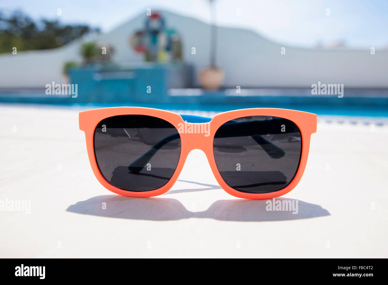 Occhiali da sole con telaio arancione al di fuori della messa a fuoco con lo sfondo della piscina Foto Stock