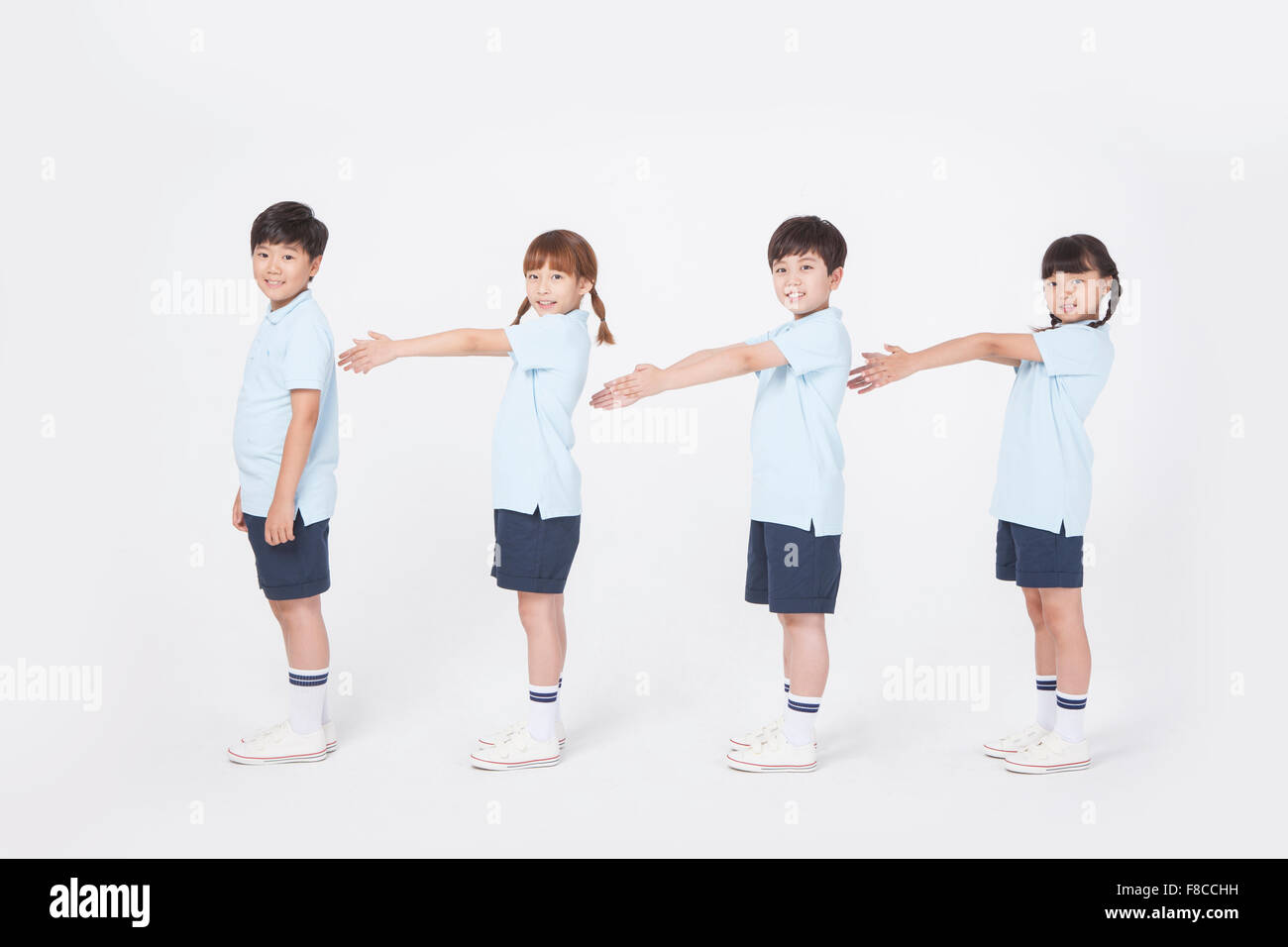 Quattro gli studenti della scuola elementare in sport uniforme lateralmente in piedi in fila e allungando le braccia in avanti per rendere una linea Foto Stock