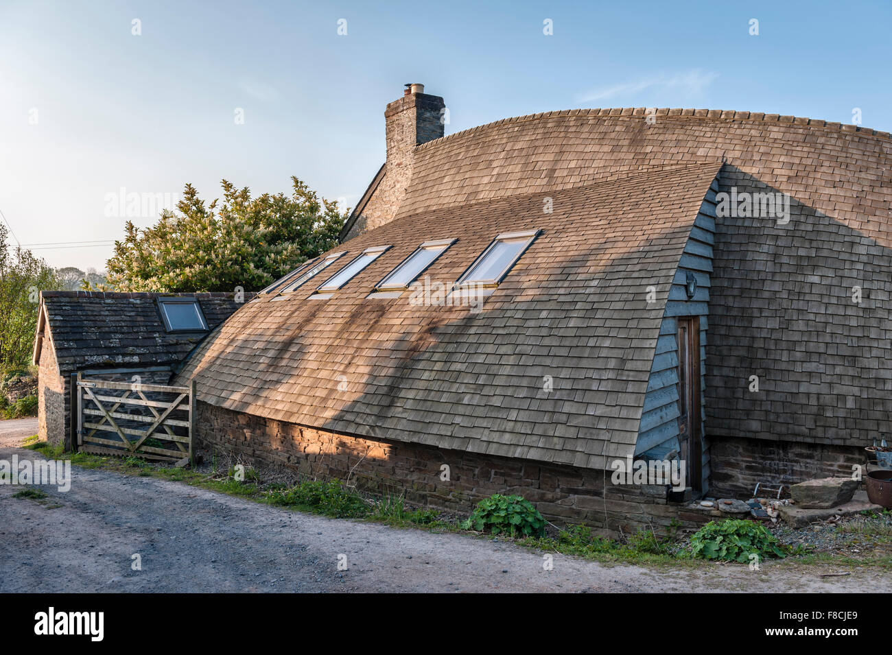 Herefordshire, Regno Unito. Un auto costruita casa, rivestita di legno con un tetto curvo con coperta in legno Scandole di cedro Foto Stock