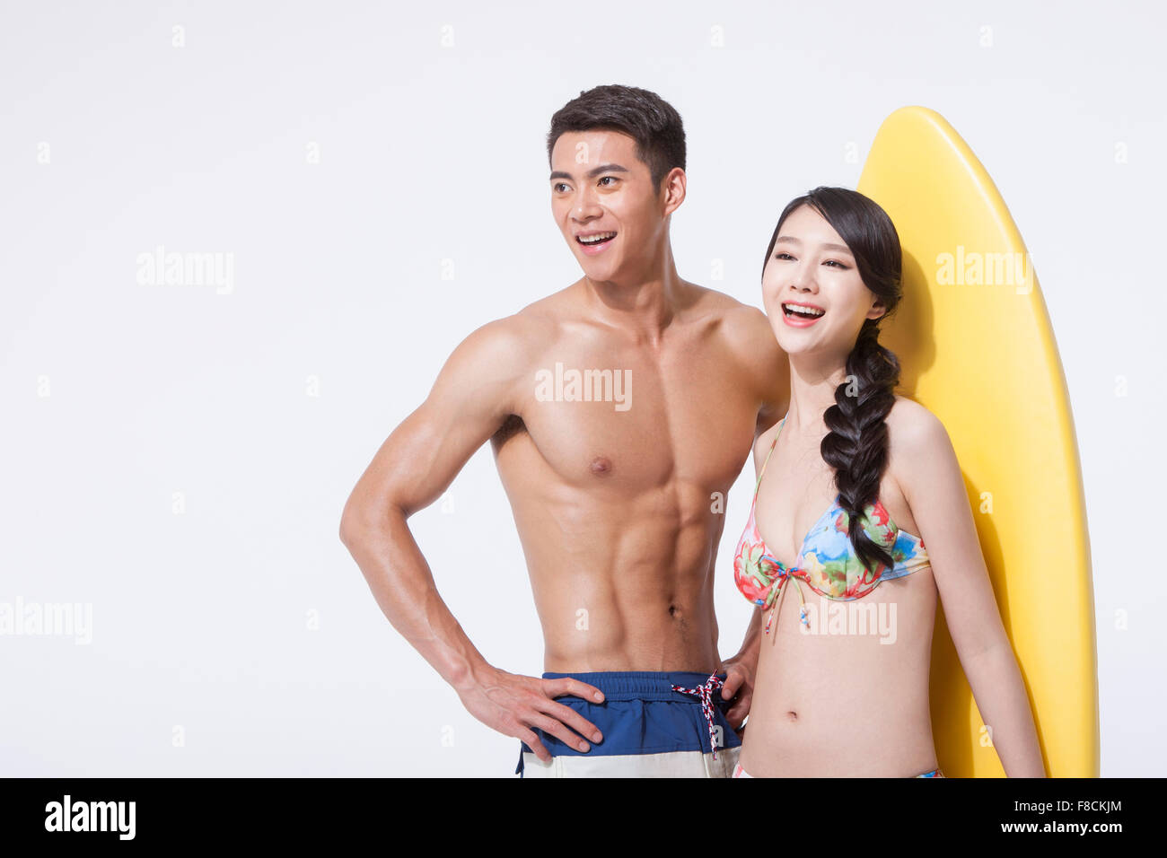 Matura in spiaggia cercando di usura in corrispondenza dell'altro lato con un sorriso e una scheda di surf dietro di loro Foto Stock
