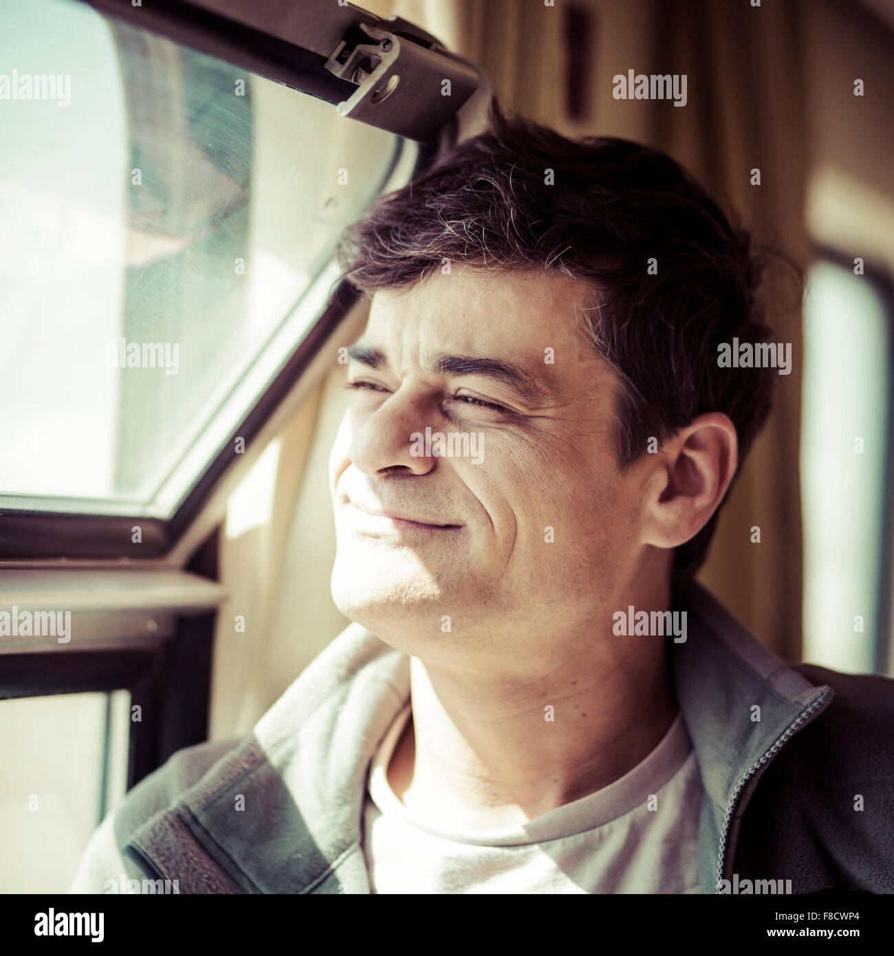 Felice l'uomo cerca attraverso la finestra del treno Shanghai-Lhasa con il sole in faccia. Foto Stock