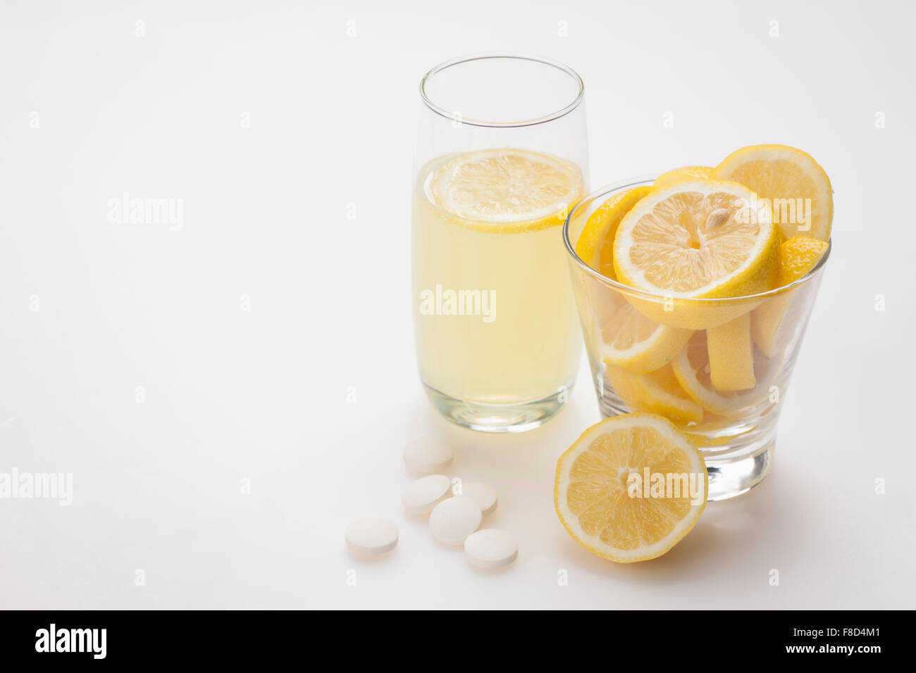 Bicchiere di limonata con una fettina di limone e fette di limone in un altro vetro e vitamina pillole posti con loro Foto Stock