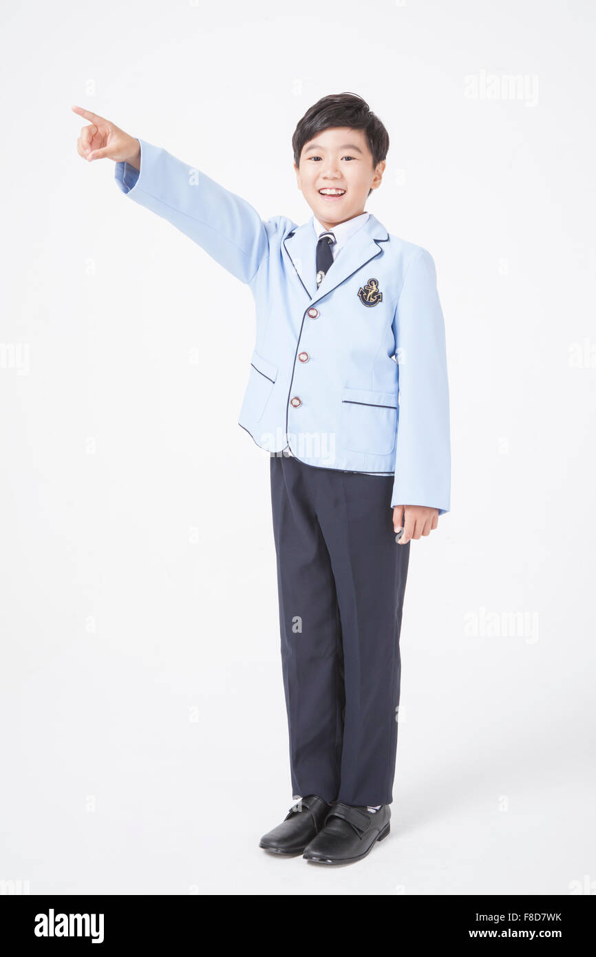 Scuola elementare ragazzo di età in uniformi di scuola puntando con il dito e in piedi Foto Stock