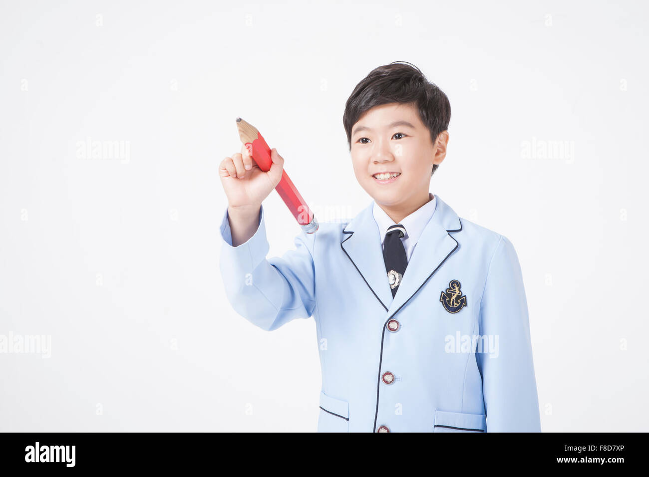 Scuola elementare ragazzo di età tenendo un grande matita rossa in mano con gesto di scrittura Foto Stock