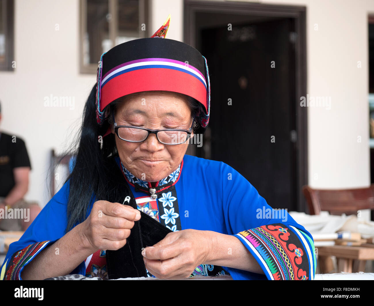 Un anziano di etnia Yi persone donna che indossa il costume tradizionale Arazzo di cucitura in disegni di Suogeyi Village, Yunnan, Cina Foto Stock