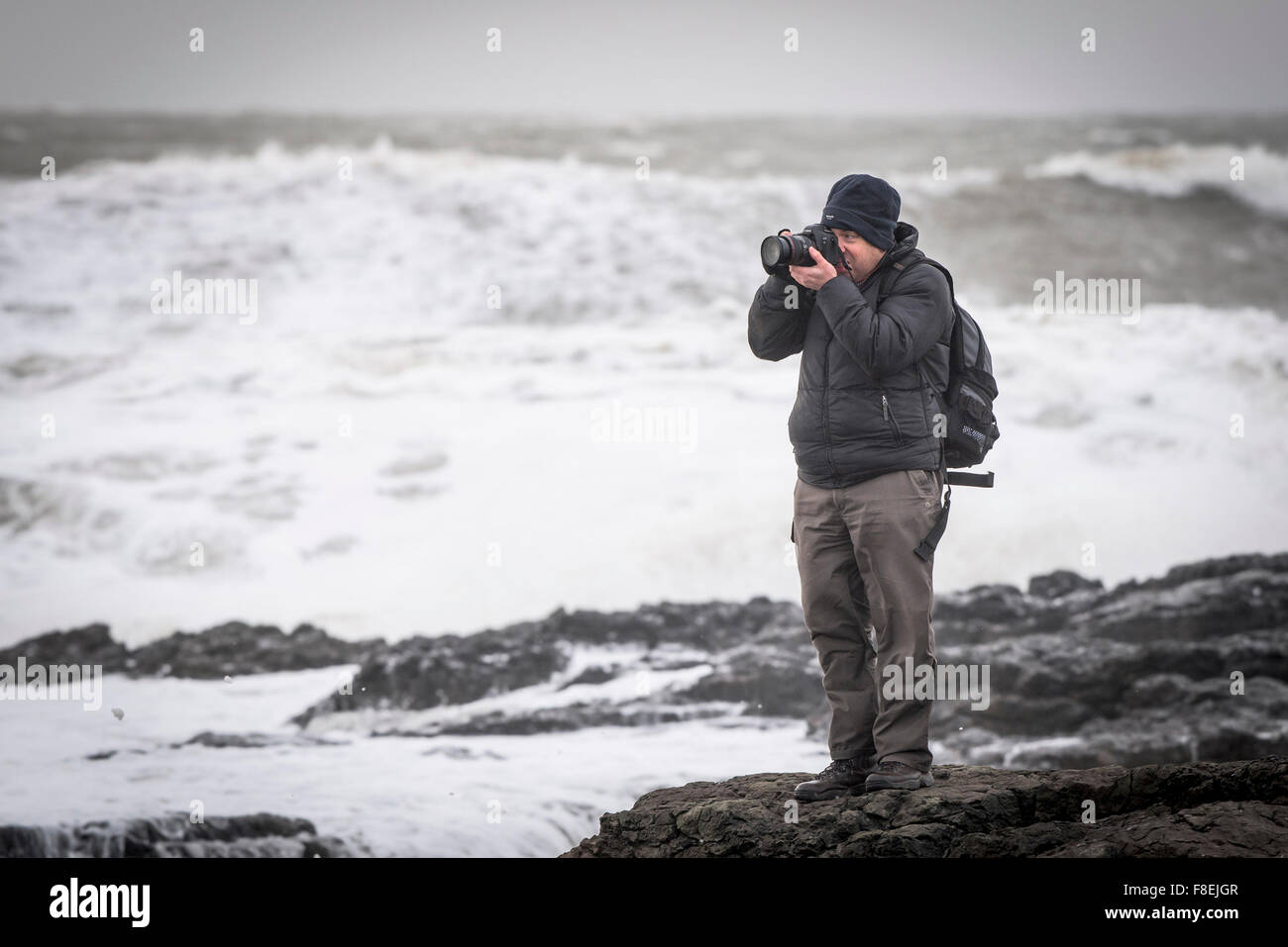 Un fotografo in piedi sulle rocce come i difficili mari di cancelletto la costa in Porthcawl, nel Galles del Sud. Foto Stock