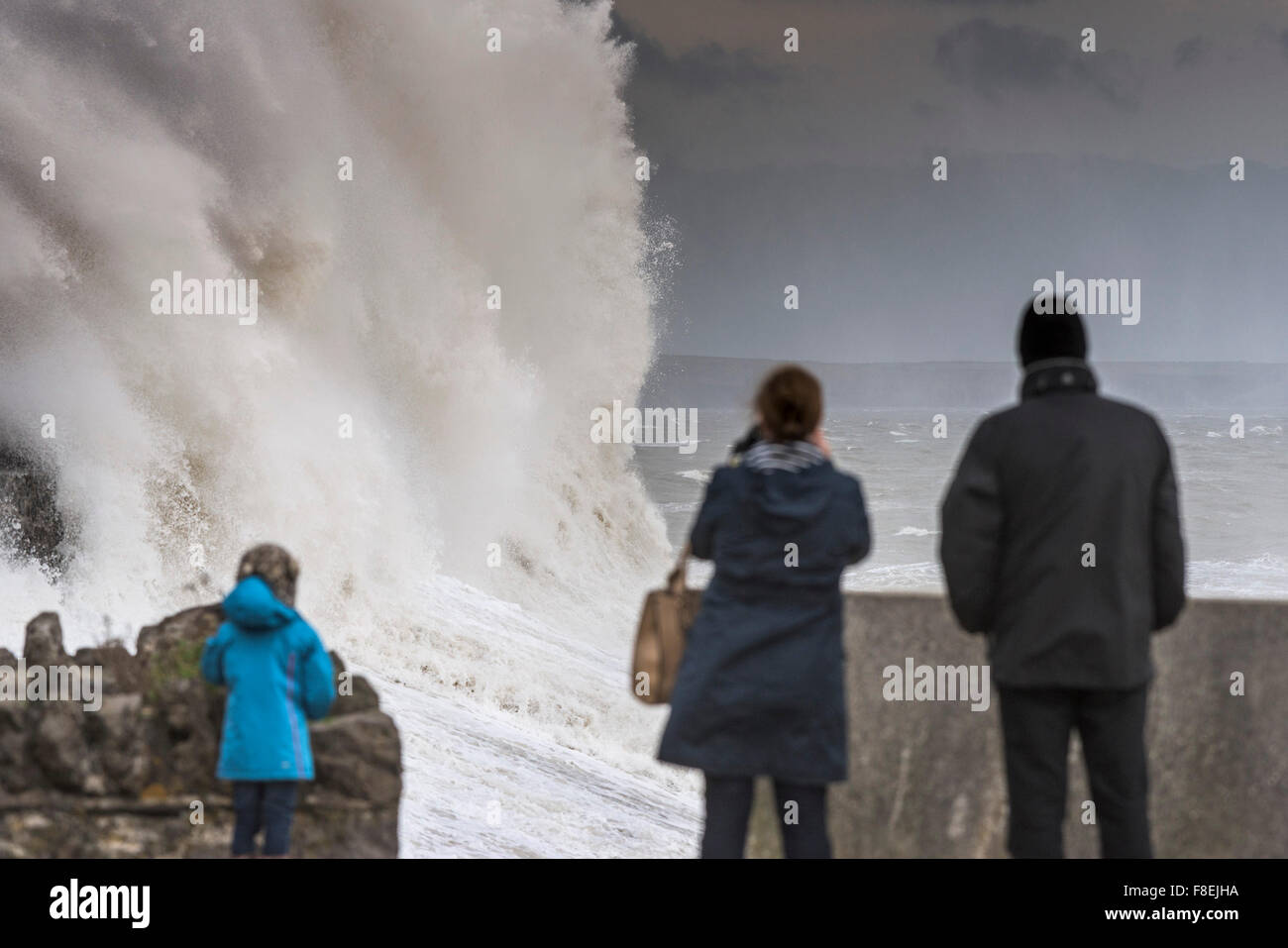 La gente guarda come enormi onde si infrangono sulla banchina e lungomare di Porthcawl, nel Galles del Sud. Foto Stock