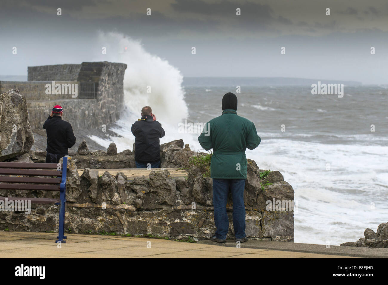 La gente guarda come grandi onde si infrangono sulla banchina sul lungomare Porthcawl nel Galles del Sud. Foto Stock
