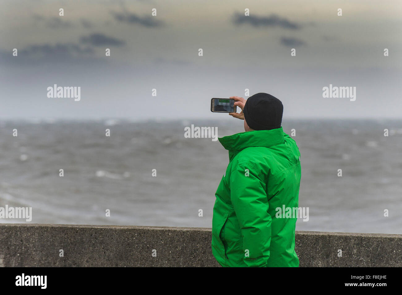 Un uomo con un telefono cellulare per fotografare il mare a Porthcawl nel Galles del Sud. Foto Stock