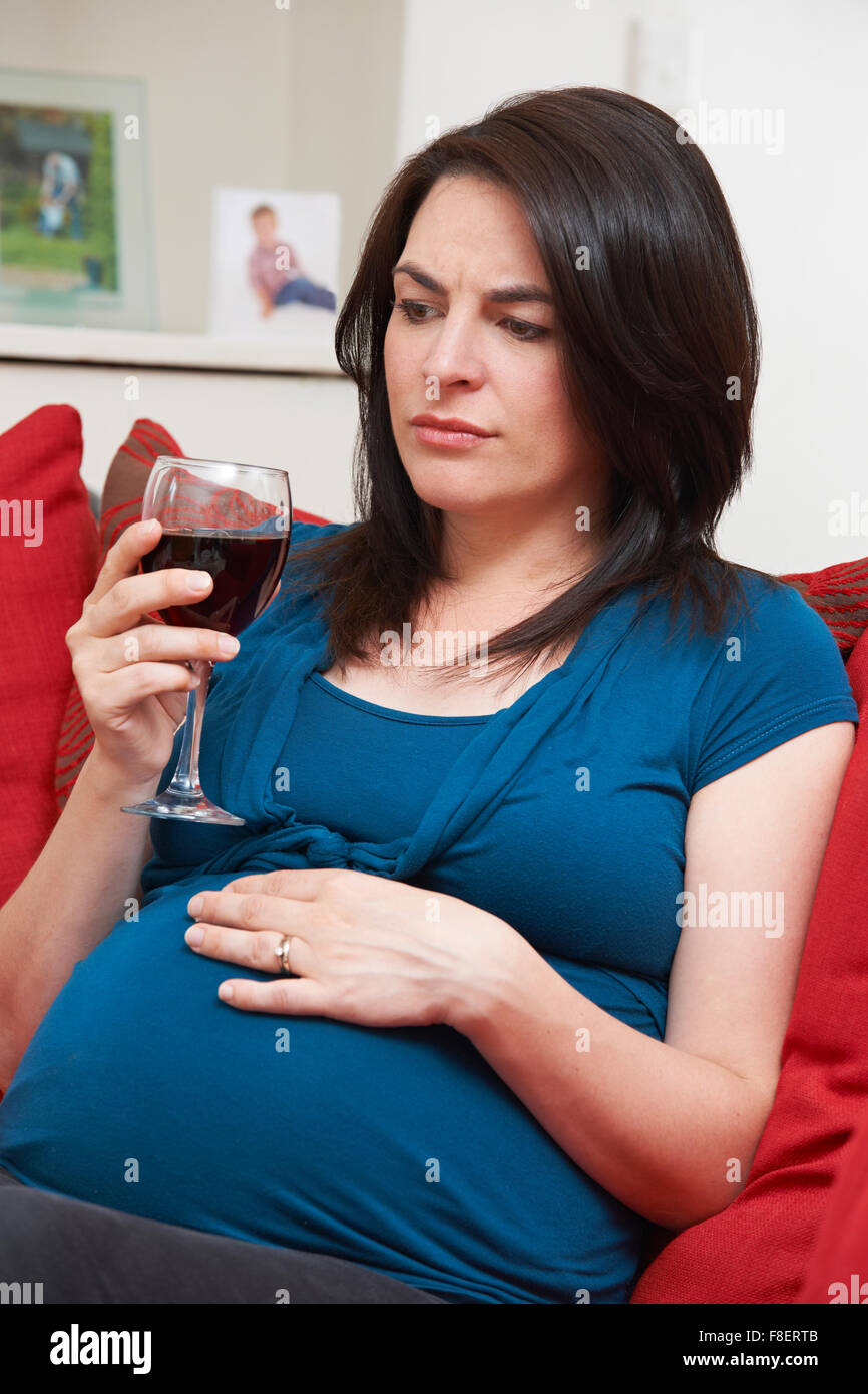 In questione donna incinta di bere un bicchiere di vino in casa Foto Stock