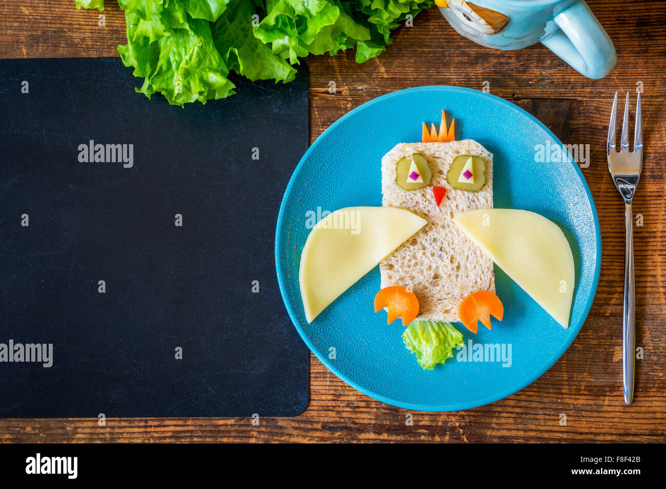 Scuola di sano il pranzo per i bambini. Funny owl sandwich e insalate sul tavolo di legno più vuoto lavagna nera per il testo. Spazio di copia Foto Stock