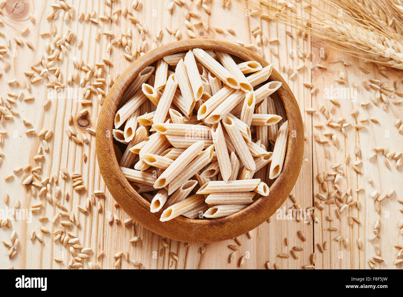 Tutta la pasta di grano in ciotola di legno circondato da grano duro sul tavolo di legno Foto Stock