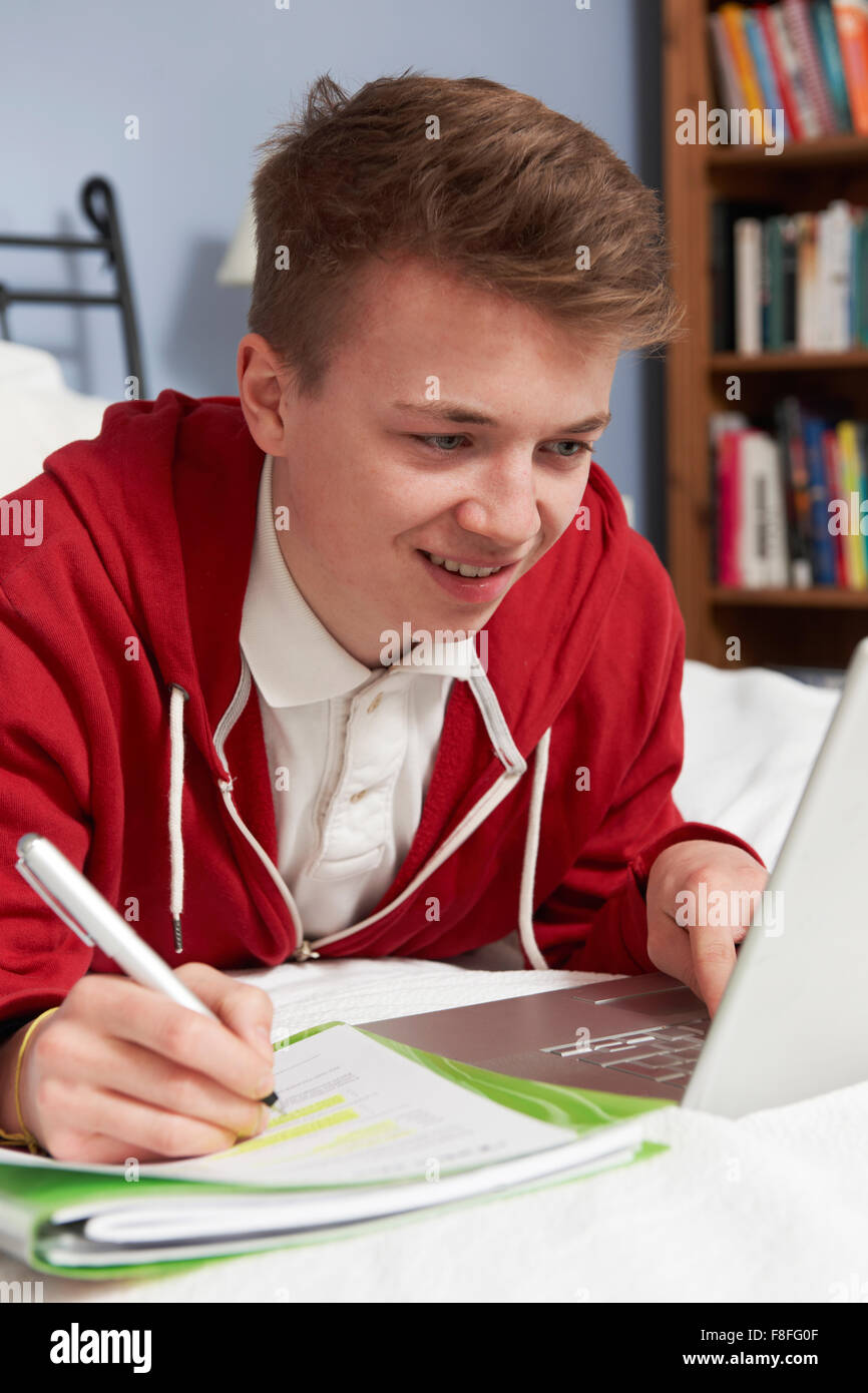 Ragazzo adolescente utilizzando computer portatile per i compiti a casa in camera da letto Foto Stock