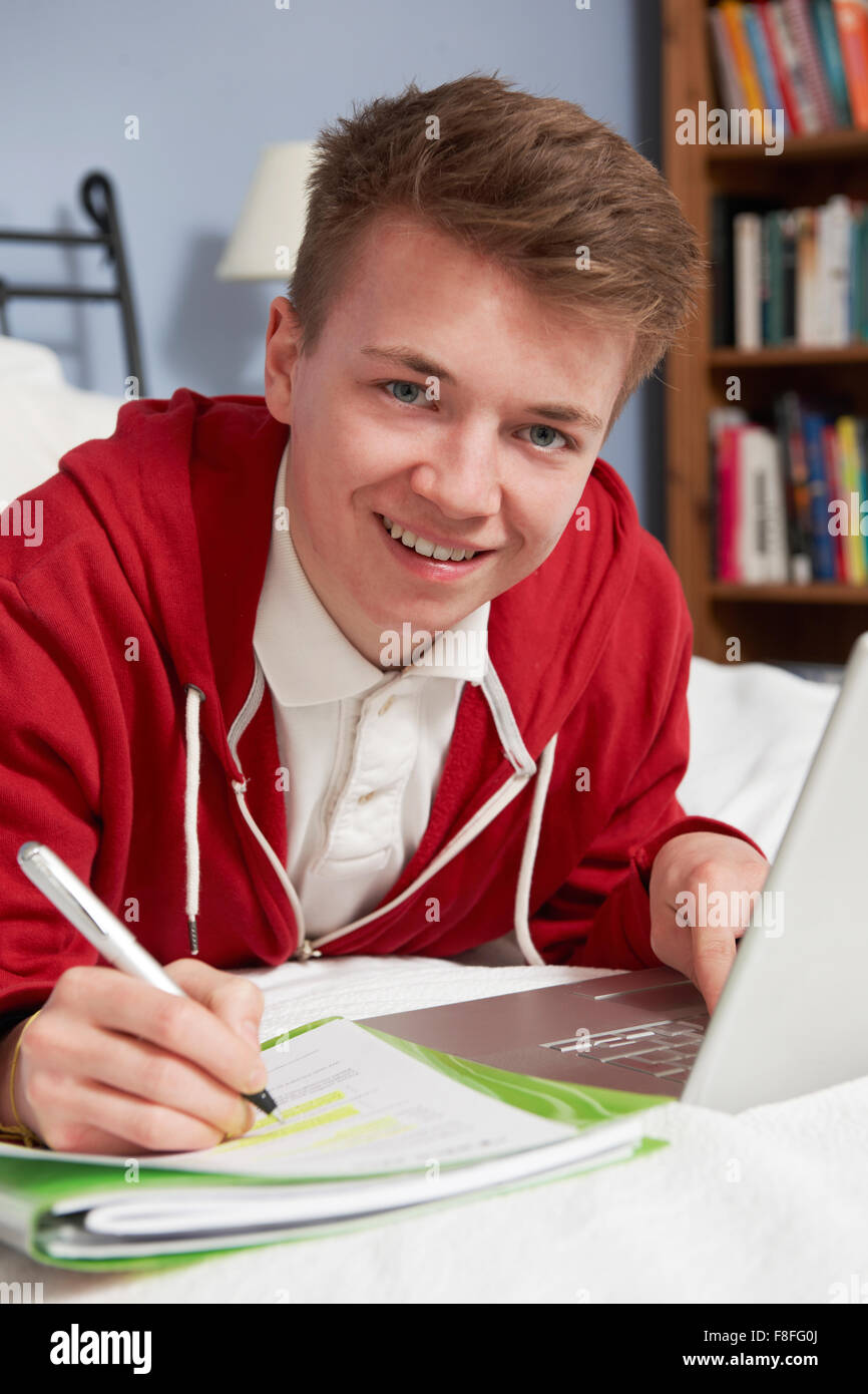 Ragazzo adolescente utilizzando computer portatile per i compiti a casa in camera da letto Foto Stock