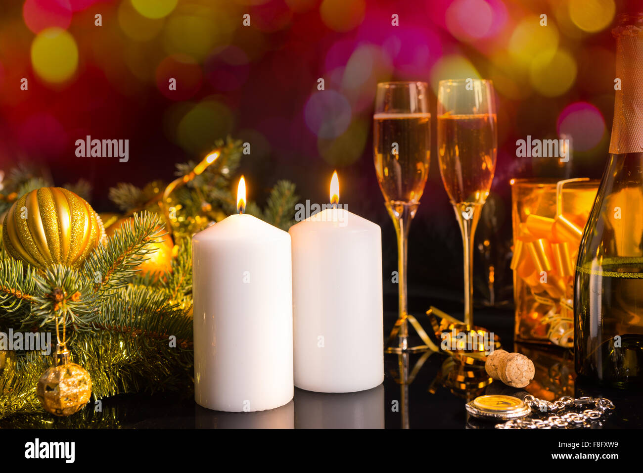 Festosa vita ancora - Due bianchi pilastro candele con la masterizzazione di stoppini sul tavolo con bicchieri di champagne e circondato con Golden decorazione di Natale accenti nella parte anteriore del background scintillanti. Foto Stock