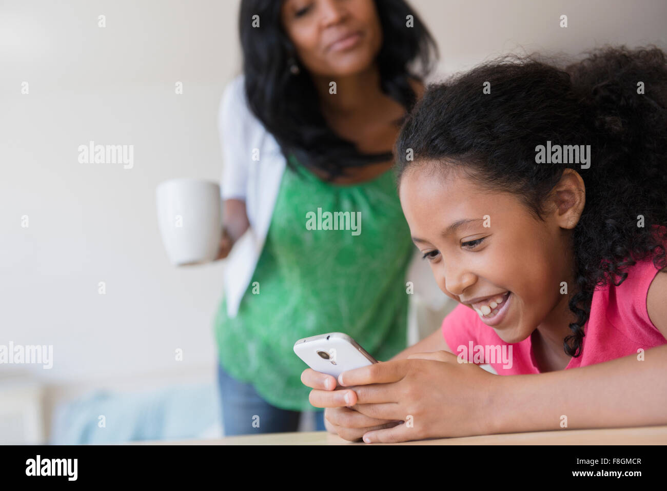 Madre guarda la figlia uso telefono cellulare Foto Stock