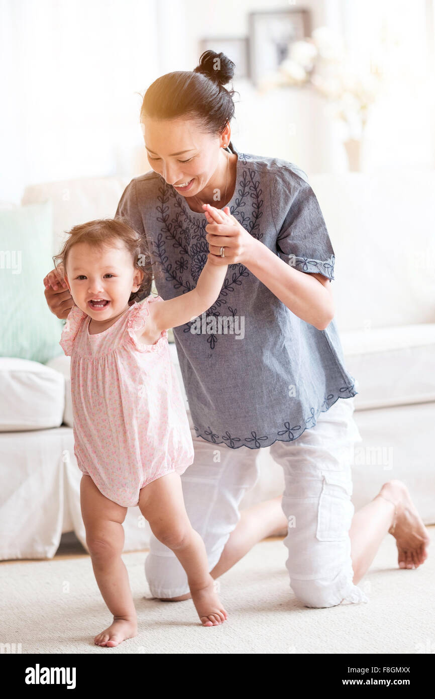 Madre aiutare la nostra bambina a piedi in salotto Foto Stock