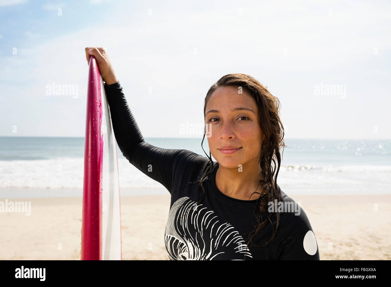 Surfista ispanica tenendo la tavola da surf in spiaggia Foto Stock